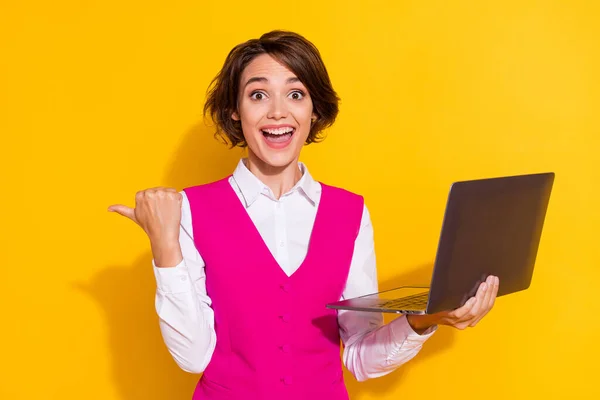 Fotografie lesklý vzrušený mladá dáma nosit růžový oblek drží moderní zařízení ukazující palec prázdný prostor s úsměvem izolované žluté barvy pozadí — Stock fotografie