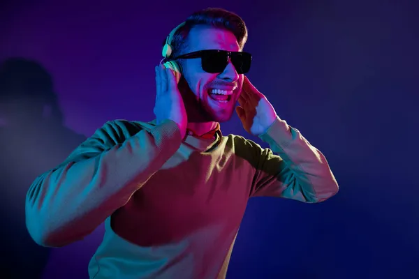 Φωτογραφία πορτρέτο του ανθρώπου που φοράει γυαλιά ηλίου ακούγοντας μουσική ακουστικά περιτριγυρισμένο απομονωμένο σκούρο πορφυρό φόντο — Φωτογραφία Αρχείου