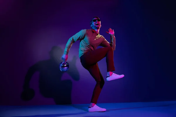 Tamanho total do corpo foto homem em vidro de sol dançando na discoteca mantendo bola de discoteca isolada no fundo cor violeta — Fotografia de Stock