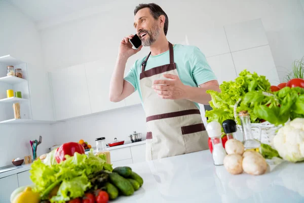 Foto de homem sociável cozinheiro ter telefonema conversa desgaste avental azul t-shirt casa cozinha dentro de casa — Fotografia de Stock
