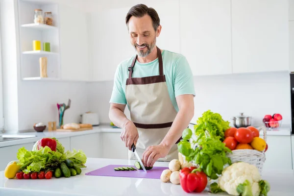 Parlak, çekici, olgun bir adamın mavi tişört giydiği, gülümseyen, yemek pişiren, sebze kesen kapalı bir ev odasında çekilmiş bir fotoğraf. — Stok fotoğraf