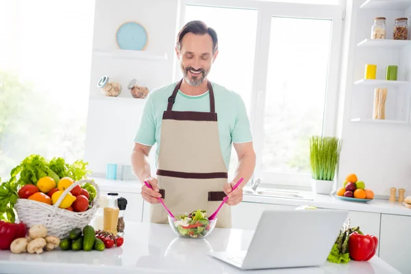 Foto av positiv stilig man mix skål sallad grepp sked bära förkläde blå t-shirt hem kök inomhus — Stockfoto