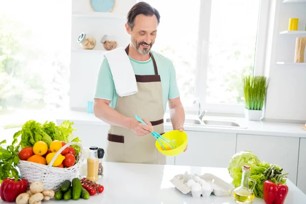 Olumlu, tatlı, olgun bir adamın mavi tişört giyip ev içinde omlet pişirirken çekilmiş fotoğrafı. — Stok fotoğraf