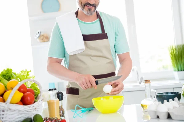 Neşeli bir adamın kesilmiş fotoğrafı yumurta kabuğu bıçağı yemek önlüğü mavi t-shirt 'ü ev mutfağında giydiriyor. — Stok fotoğraf