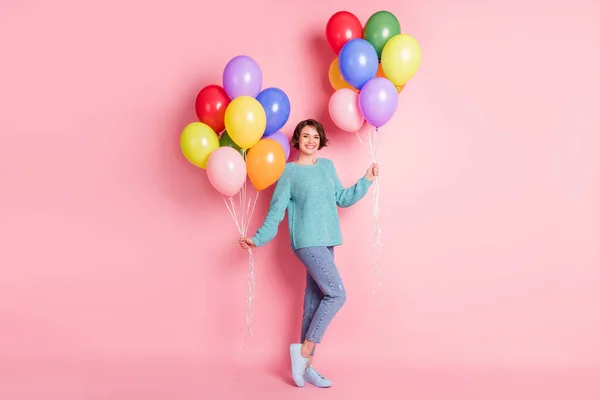 Full size foto di ottimistico riccio bruna acconciatura signora tenere palloncini indossare blu maglione jeans scarpe da ginnastica isolato su sfondo di colore rosa — Foto Stock