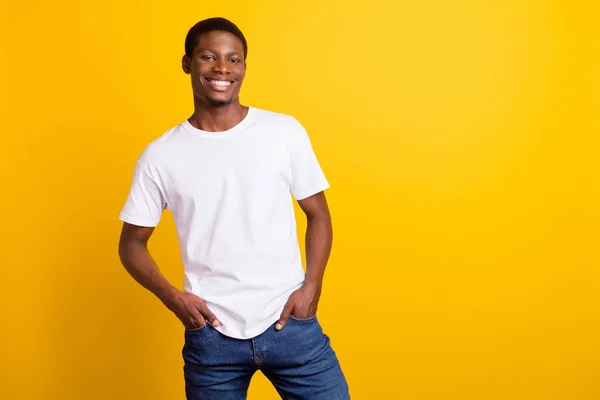 Foto van vrolijke jonge donkere huid vrolijke man houd handen jeans zakken geïsoleerd op glans gele kleur achtergrond — Stockfoto