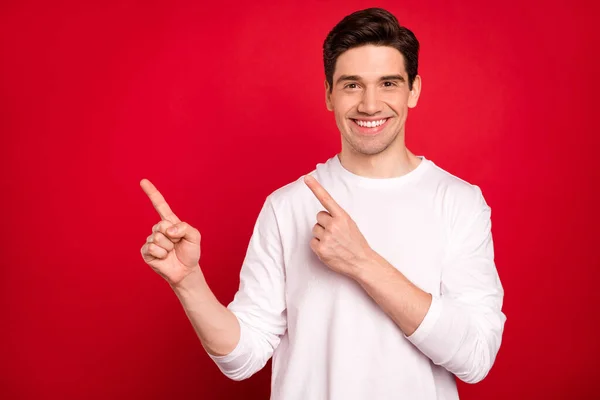 Foto van grappige brunet millennial guy point lege ruimte dragen witte shirt geïsoleerd op rode kleur achtergrond — Stockfoto