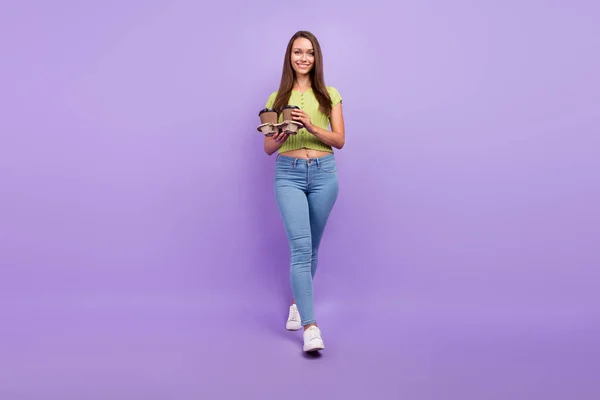 Вид в полный рост на прекрасную жизнерадостную девушку, держащую в руках латте, идущую в изоляции на фоне фиолетового цвета — стоковое фото