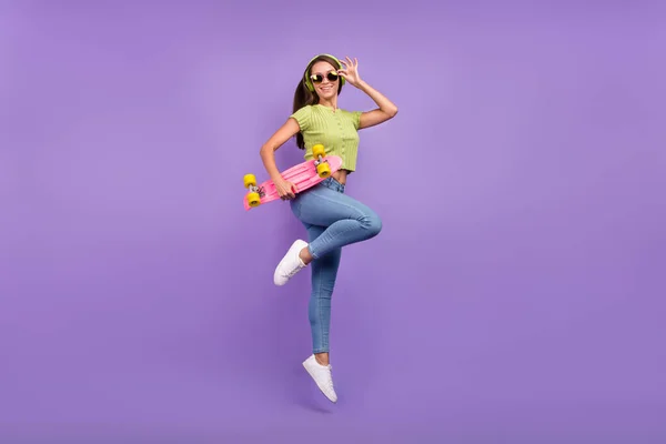 Lunghezza completa dimensione del corpo vista di bella allegra ragazza che salta ascoltando pop dancing con skate isolato su viola viola colore sfondo — Foto Stock