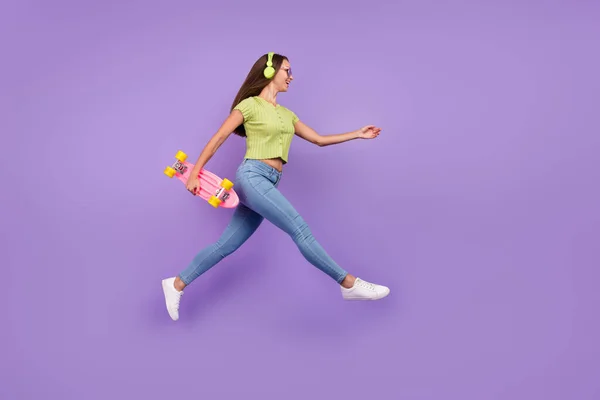 Ganzkörpergröße Ansicht von netten fröhlichen Mädchen springen Hören einzigen Hit gehen mit Schlittschuh isoliert über lila Farbe Hintergrund — Stockfoto
