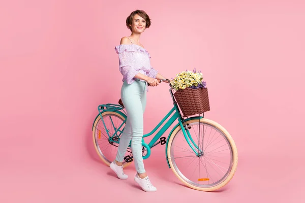 Foto em tamanho completo de jovens felizes positivo alegre sorridente menina segurar bicicleta com flores silvestres isoladas no fundo cor-de-rosa — Fotografia de Stock