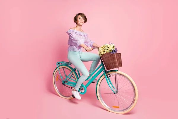 Foto de bicicleta drive senhora positiva entregar flores usar calças de blusa violeta sapatos isolado cor rosa fundo — Fotografia de Stock