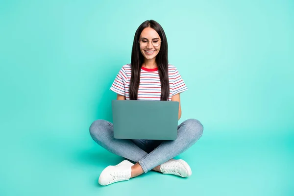 Full size foto di bella signora ottimista lavoro computer portatile indossare occhiali t-shirt jeans scarpe da ginnastica isolato su sfondo color verde acqua — Foto Stock