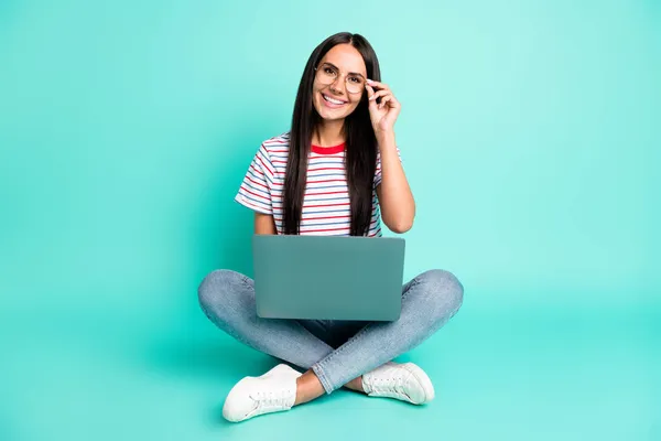 Full size foto di bella signora ottimista lavoro laptop sedersi indossare occhiali t-shirt jeans scarpe da ginnastica isolato su sfondo color verde acqua — Foto Stock