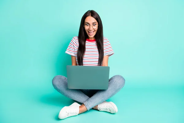 Pełny rozmiar zdjęcie pod wrażeniem brunetka fryzjerka pani siedzieć pisać laptop nosić t-shirt dżinsy trampki izolowane na ciemnym tle — Zdjęcie stockowe