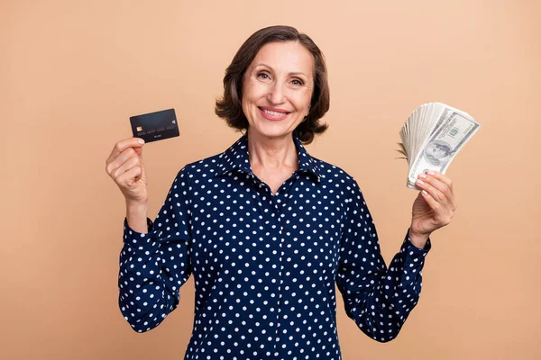 Foto di bel capo invecchiato bruna signora tenere i soldi della carta usura camicia punteggiata isolato su sfondo di colore beige — Foto Stock