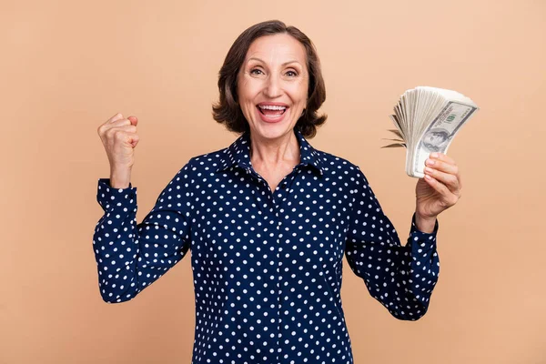 Foto di cool vecchia signora bruna tenere i soldi urlare indossare camicetta punteggiata isolato su sfondo di colore beige — Foto Stock