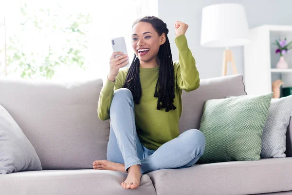 Foto de cuerpo completo de la joven mujer feliz sentarse sofá mirada teléfono ganador dentro de casa casa interior — Foto de Stock