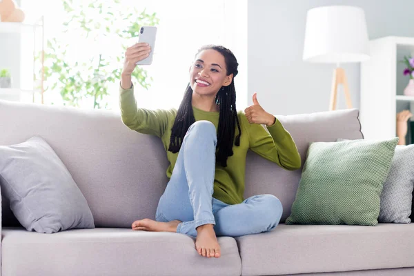 Фото милой блестящей леди носить зеленый пуловер сидя диван показывая большой палец вверх принимая селфи современный гаджет в помещении домашний дом — стоковое фото
