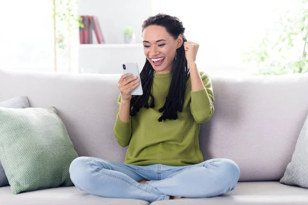 Foto de longitud completa de alegre afro americano feliz levantamiento de puño ganador sostener teléfono de la mano en el interior de casa casa — Foto de Stock