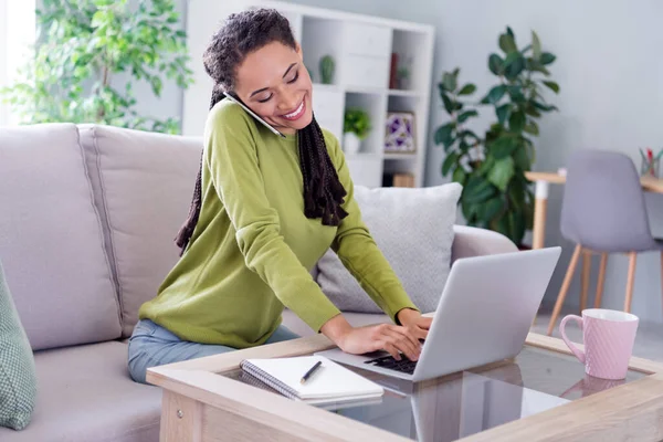 Foto de joven alegre feliz mujer positiva escribir portátil hablar de teléfono en el interior de casa casa — Foto de Stock