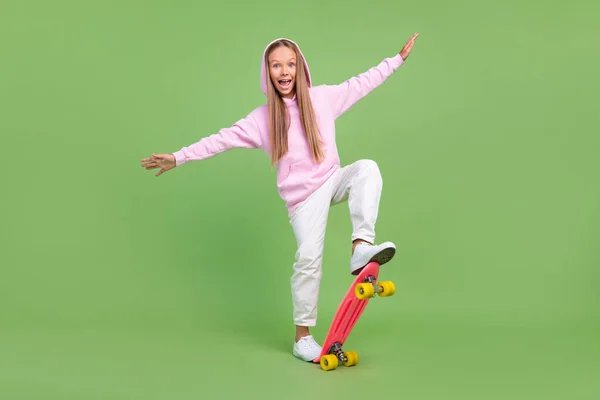 Foto de cuerpo completo de la niña rubia funky paseo skate desgaste sudadera con capucha pantalones zapatillas aisladas sobre fondo verde — Foto de Stock