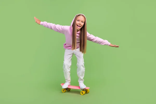 Full kropp foto av imponerad liten blond flicka rida skridsko bära hoodie byxor sneakers isolerad på grön bakgrund — Stockfoto