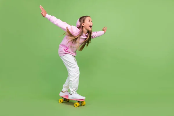 Full length photo of impressed little blond girl ride skate wear hoodie trousers sneakers isolated on green background — Stock Photo, Image