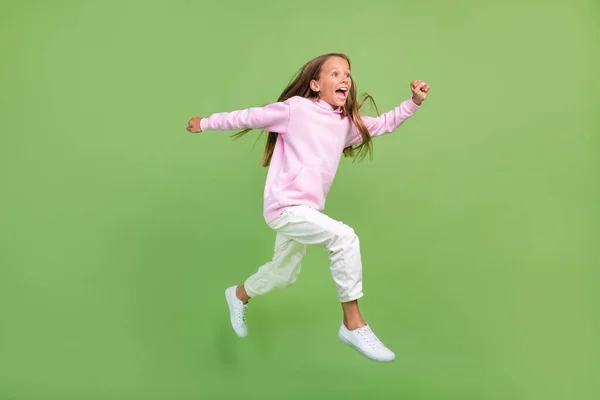 금발 소녀가 뛰고 있는 전체 길 이 사진 녹색 배경에 고립된 스웨트 셔츠 바지 운동화를 착용 — 스톡 사진