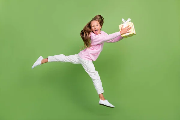Foto de perfil de longitud completa de la pequeña chica rubia impresionada correr celebrar regalo desgaste sudadera pantalones zapatillas aisladas sobre fondo verde — Foto de Stock