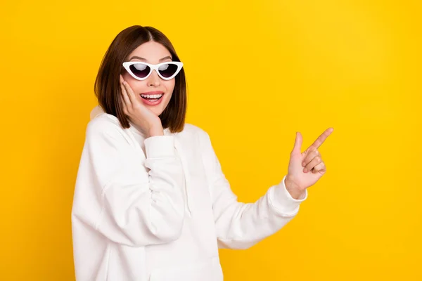 Photo of excited promoter lady indicate finger empty space wear sunglass white hoodie isolated yellow color background — Stock Photo, Image