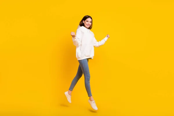 Foto de senhora surpreendida salto alegrar-se ganhar desgaste branco sweatshirt jeans tênis isolado cor amarela fundo — Fotografia de Stock