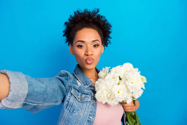 Genç esmer kadının fotoğrafı kot ceket giyer selfie 'ye hava öpücüğü gönderir mavi arka planda izole çiçekler. — Stok fotoğraf