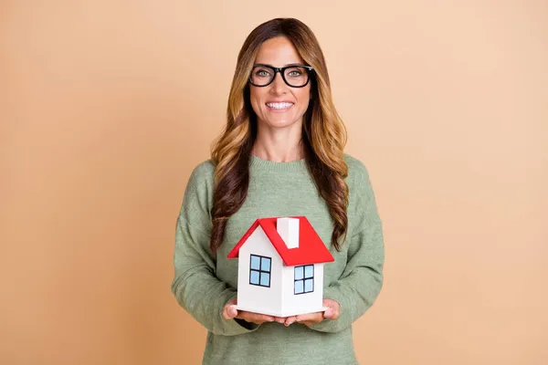 Fényképezés portré nő visel szemüveg mosolygós tartása kis ház elszigetelt pasztell bézs szín háttér — Stock Fotó