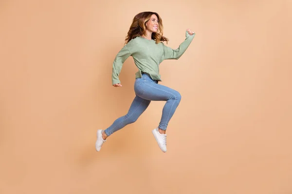 フル長さボディサイズ写真女性ジャンプ高実行陽気で幸せなカジュアル服孤立パステルベージュ色背景 — ストック写真
