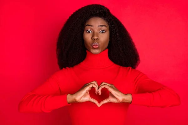 Фотографія молодої африканської жінки кинуті губи посилають повітряний поцілунок, показують пальці серця символ любові ізольовані на фоні червоного кольору — стокове фото