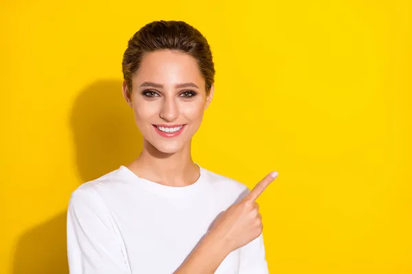 Foto av optimistisk brun kort frisyr ung dam punkt tomt utrymme bära vit t-shirt isolerad på gul färg bakgrund — Stockfoto