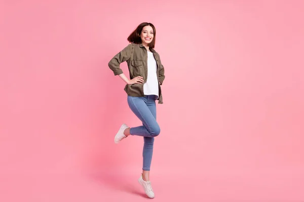 Foto de tamaño completo de cool morena peinado señora salto usar pantalones vaqueros camisa caqui zapatillas aisladas en el fondo de color rosa —  Fotos de Stock