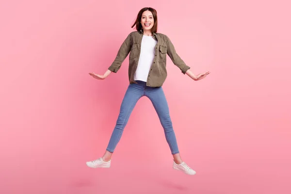 Foto de longitud completa de divertido peinado morena señora salto desgaste camiseta verde jeans zapatillas aisladas sobre fondo de color rosa —  Fotos de Stock