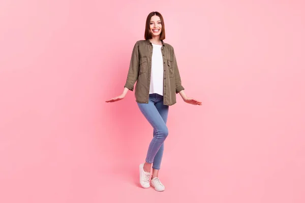 Foto de cuerpo entero de la divertida morena peinado señora stand usar camisa verde jeans zapatillas aisladas en el fondo de color rosa —  Fotos de Stock