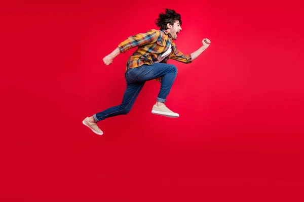 Foto von ziemlich charmanten jungen Herrn tragen kariertes Outfit lächelnd springen hoch läuft schnell isoliert rote Farbe Hintergrund — Stockfoto