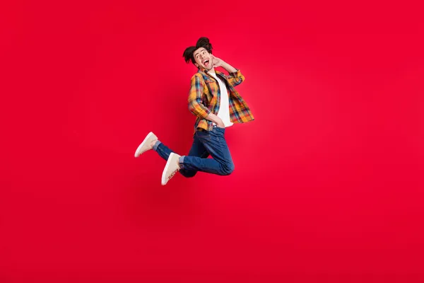 Photo of sweet attractive guy dressed checkered clothes jumping high looking back empty space isolated red color background — Stock Photo, Image