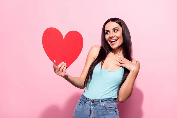Foto portrét hezká bruneta ohromen vedení srdce pohlednice s úsměvem izolované pastel růžová barva pozadí — Stock fotografie
