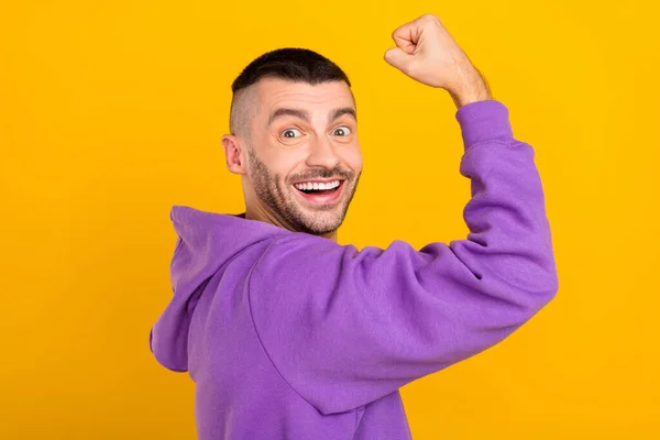 Foto porträtt ung man bär lila hoody visar starka biceps isolerad levande gul färg bakgrund — Stockfoto