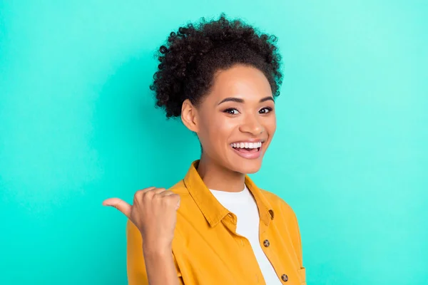 Foto de mulher bonita animado usar camisa amarela apontando polegar de volta espaço vazio sorrindo isolado fundo cor teal — Fotografia de Stock