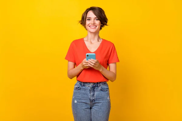 Foto de adorable amigable chica manos sostener teléfono radiante sonrisa mirada cámara aislada sobre fondo de color amarillo — Foto de Stock