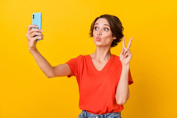 Foto von netten brünetten optimistischen Dame tun Selfie Schlag Kuss zeigen V-Zeichen tragen rotes T-Shirt isoliert auf lebendigen gelben Hintergrund — Stockfoto