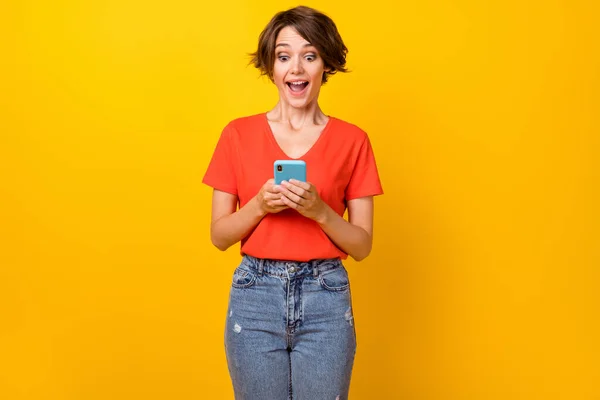 Foto van mooie brunette onder de indruk dame kijken telefoon dragen rood t-shirt geïsoleerd op levendige gele kleur achtergrond — Stockfoto