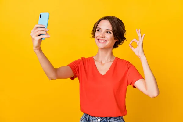 Foto de boa morena otimista senhora do selfie mostrar okey sinal desgaste vermelho t-shirt isolado no fundo de cor amarelo vívido — Fotografia de Stock