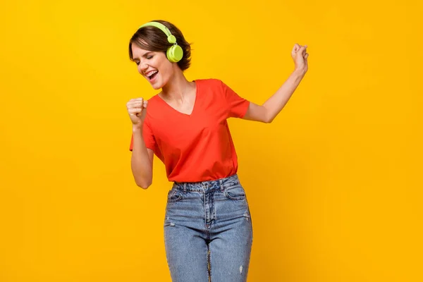 밝은 갈색 머리의 여성 댄스 가수가 노래하는 음악을 듣는 사진, 선명 한 노란색 배경에 고립된 헤드폰빨간 티셔츠를 입고 있다 — 스톡 사진